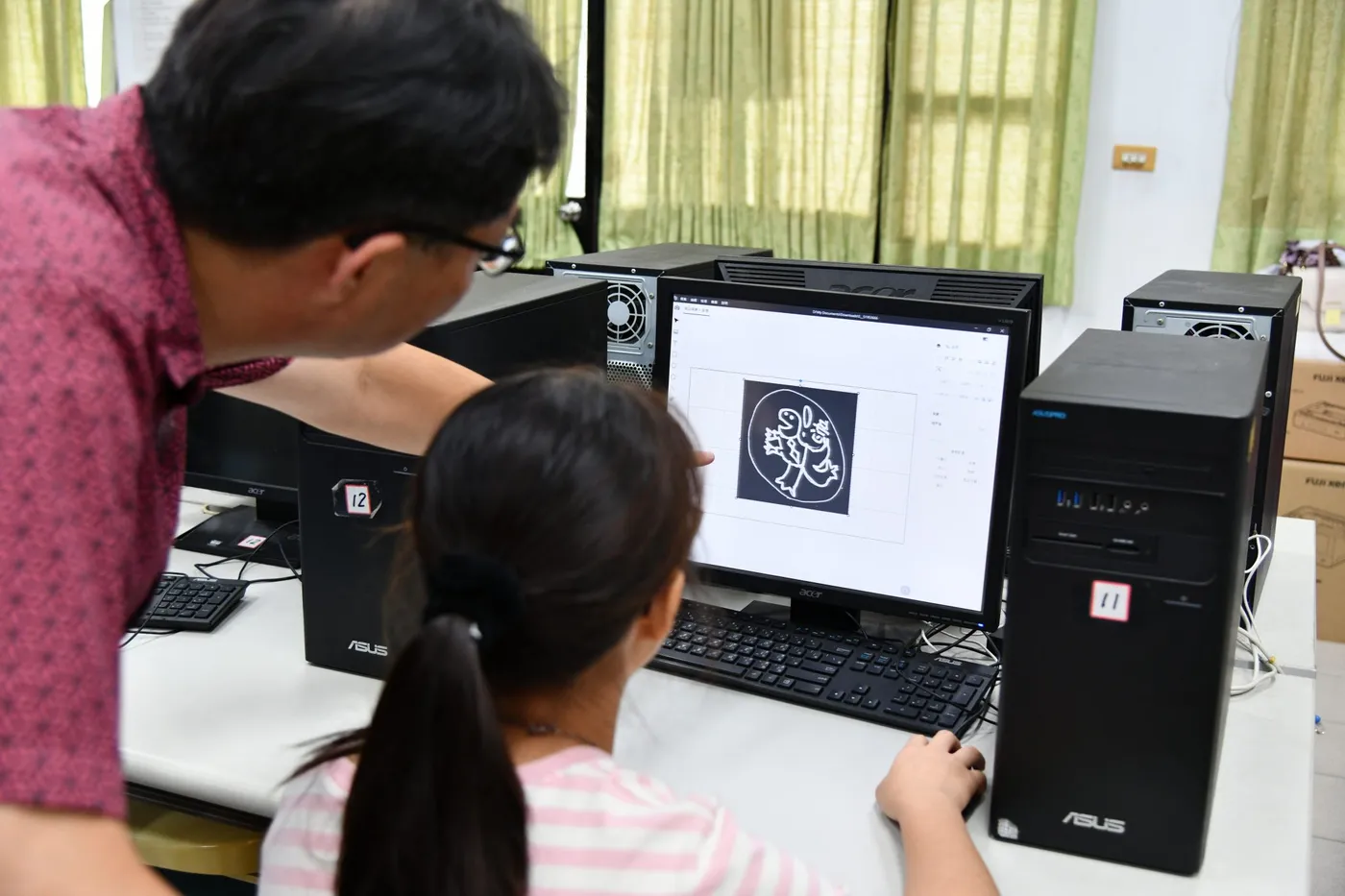 老師指導學生在教室電腦上準備圖稿